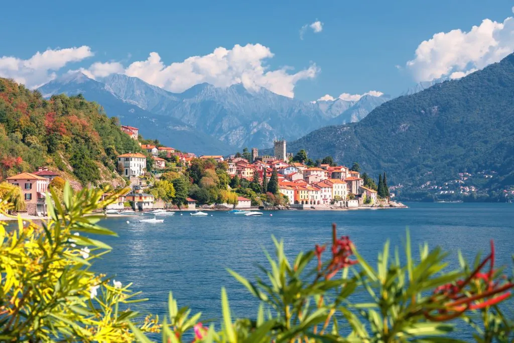 Malcesine italy as seen from across the water with greenery in the foreground and mountains behind the village