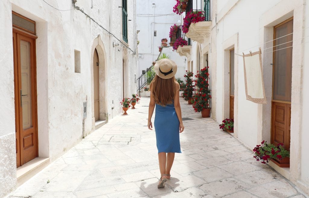 young woman in a blue dress walking along a whitewashed street in Locorotondo, one of the best italian villages to visit