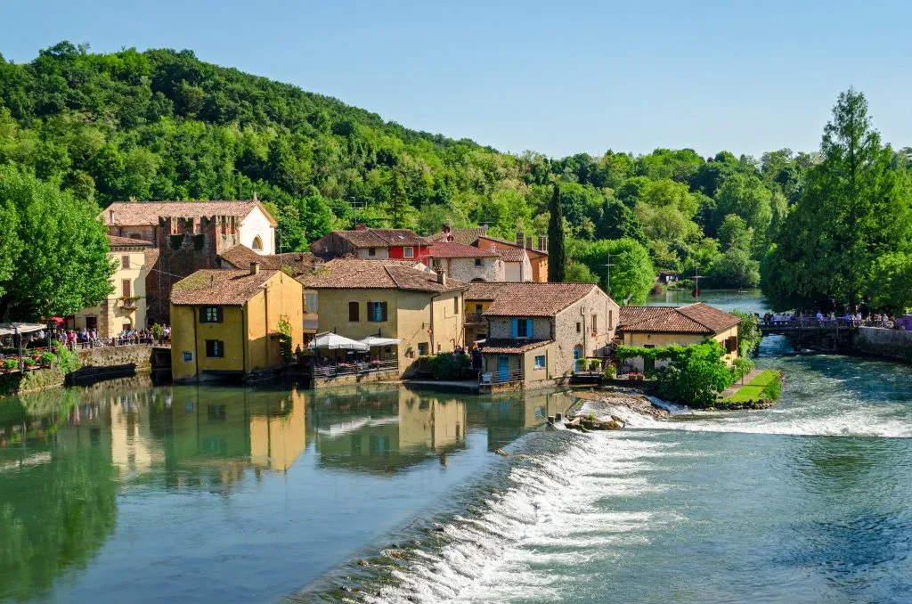 small italian village of Borghetto sul Mincio as seen from across the water, with a very small waterfall in the foreground