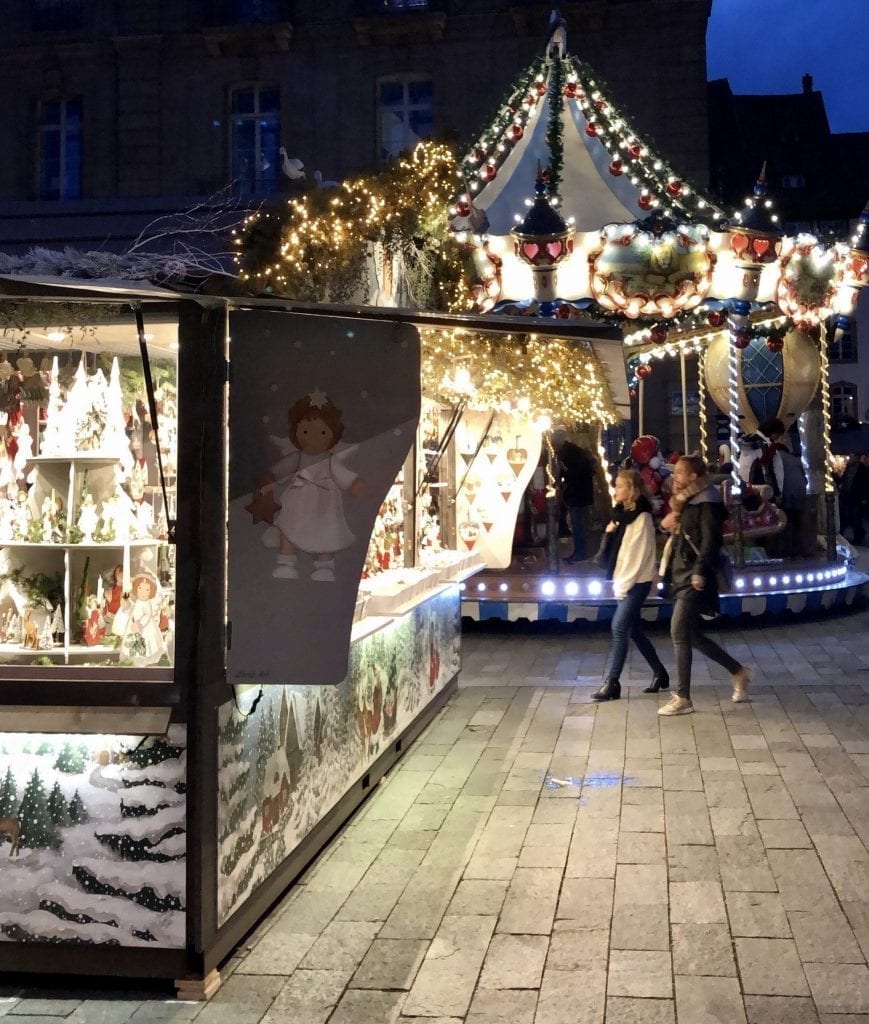 Christmas market stall with carousel and a couple walking in the background at night in Strasbourg in December