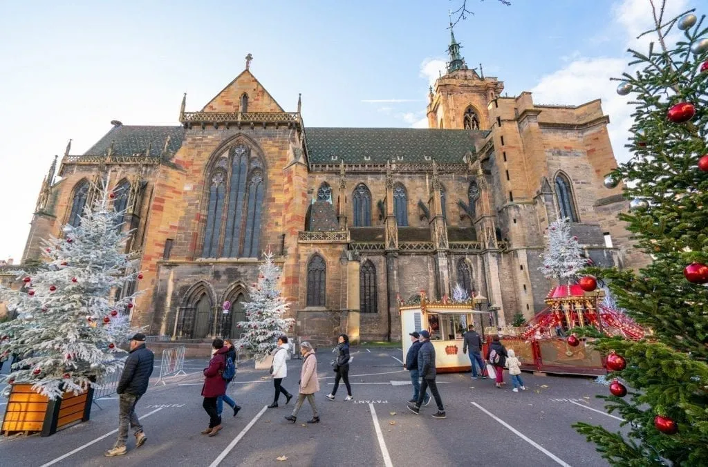 Church in Colmar in winter with Christmas trees and children's ride set up in front of it