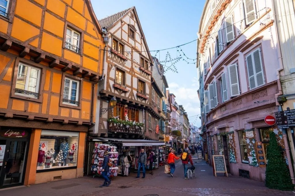 Street in Colmar France with storefronts decorated on either side for Christmas