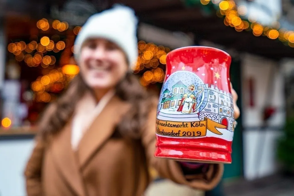 Kate Storm holding a red mug out to the camera at a Cologne Christmas market, home to some of the best Christmas markets in Europe