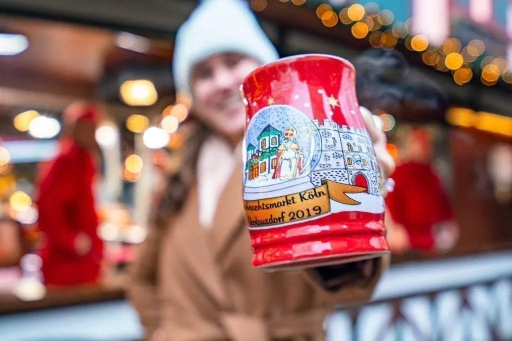 Kate Storm holding a red mug out to the camera at a Cologne Christmas market, home to some of the best Christmas markets in Europe