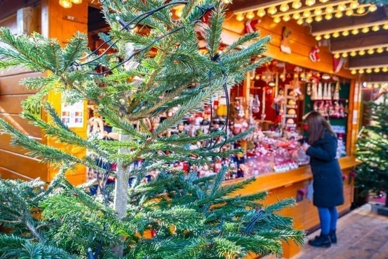 close up of a christmas market stall behind a tree with someone shopping, a typical view during a christmas in europe itinerary