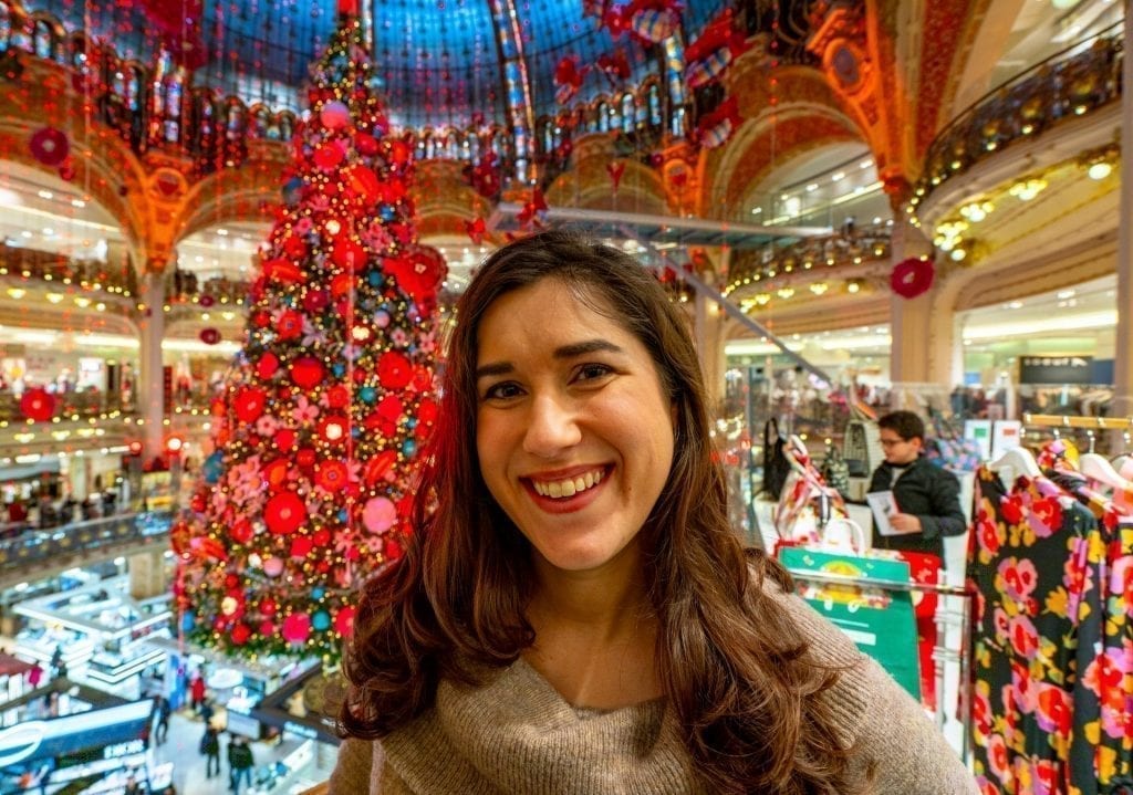 Kate Storm in a brown sweater in front of the 2019 Galeries Lafayette Christmas tree in Paris