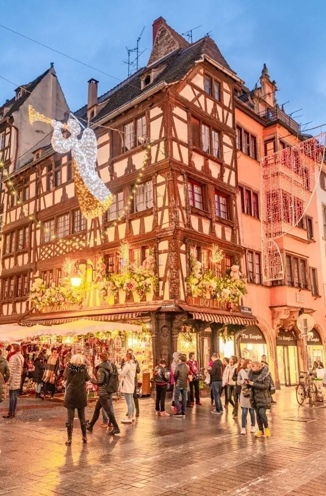 Crowd of people crossing the street in Strasbourg in December in front of a beautiful half-timbered house with Christmas lights