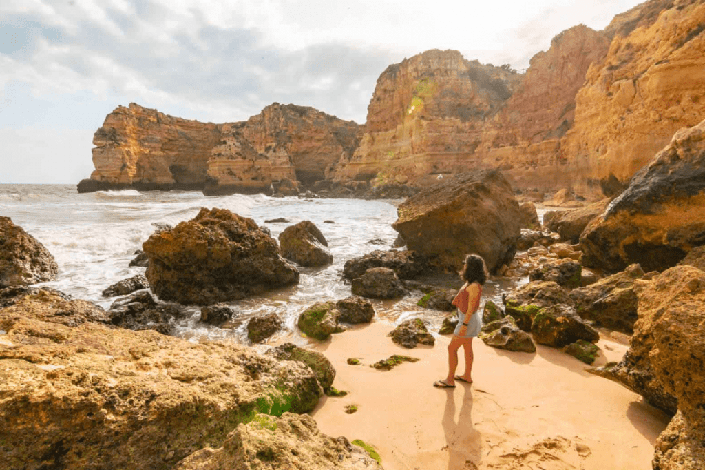 Woman standing on a rocky beach on the Algarve Coast, one of the best road trips in Europe
