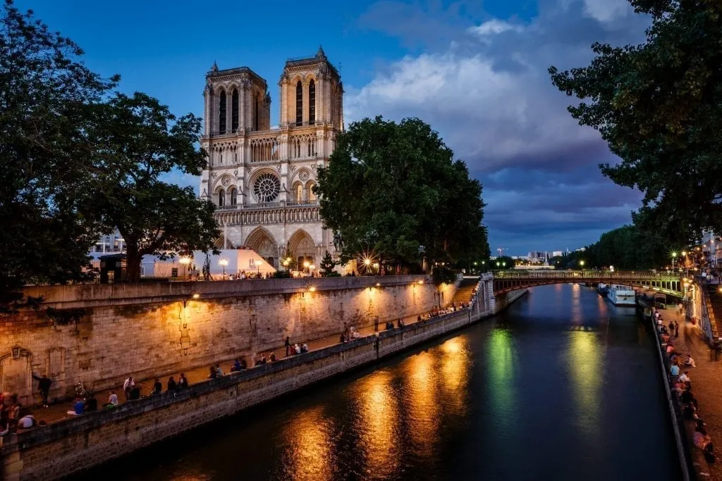 Seine River in Paris at night with Notre Dame visible on the left. Strolling along the Seine is one of the most classic things to do in Paris at night.