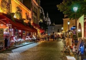 Montmartre street scene with cafes to the left. Montmartre is one of the best neighborhoods to visit when deciding what to do in Paris at night