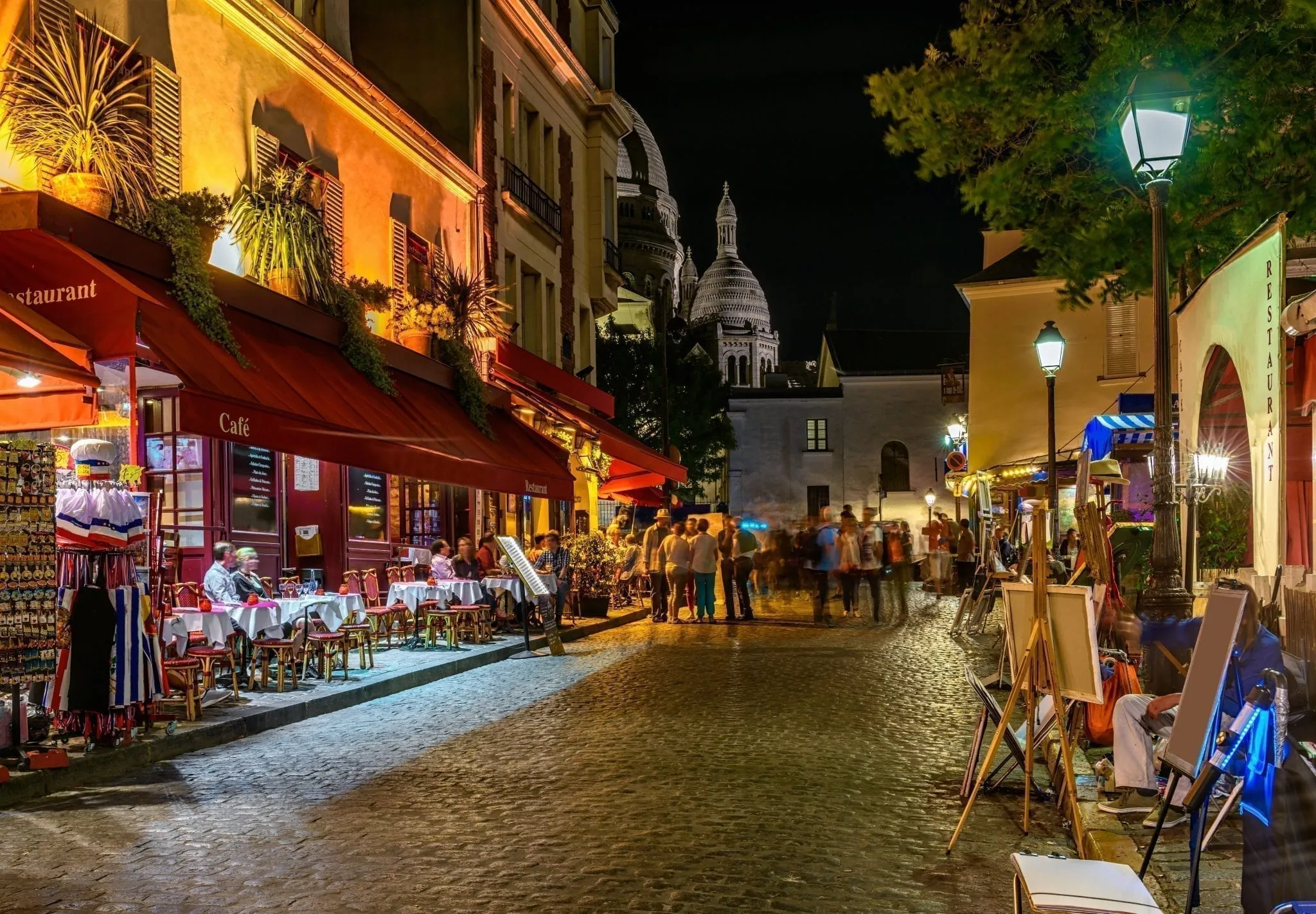 Montmartre street scene with cafes to the left. Montmartre is one of the best neighborhoods to visit when deciding what to do in Paris at night