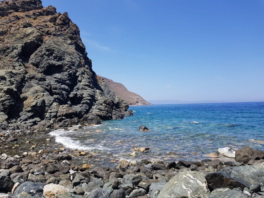 Volcanic beach in eastern Crete with bright blue water and black, rocky sand