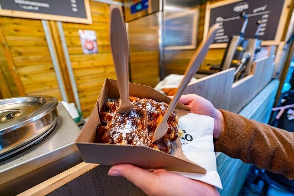 kate storm holding out a belgian waffle at a belgium christmas market