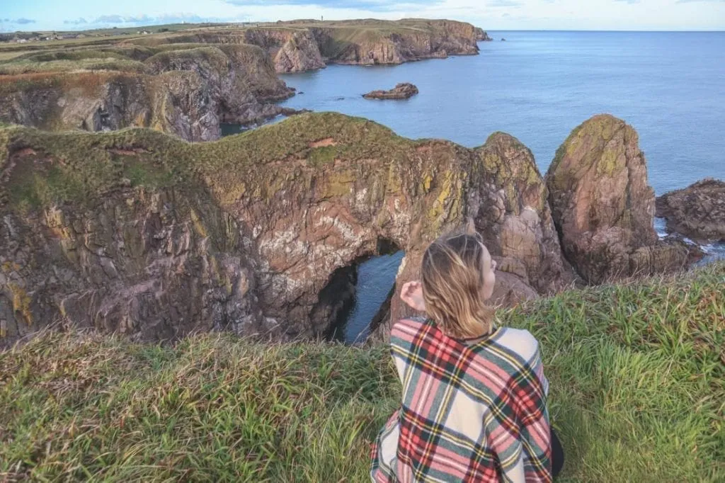 Gemma Armit wearing tartan and looking out over a cliff on the east coast of Scotland