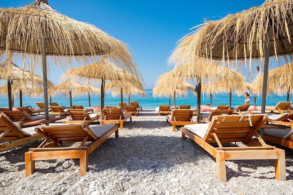 Beach chairs and umbrellas facing toward the bright sea on the Albanian Riviera, as seen as part of a Europe road trip itinerary