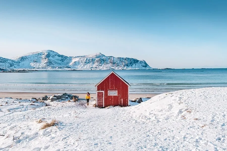 Snowy beach in Lofoten Norway as seen during a northern Europe road trip, with a small red building in the center of the photo