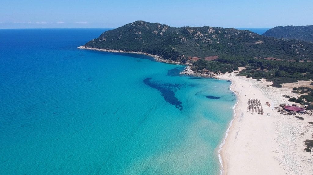 White sand beach of Sardinia as seen from above when driving through Sardinia, with turquoise water visible on the left side of the photo.