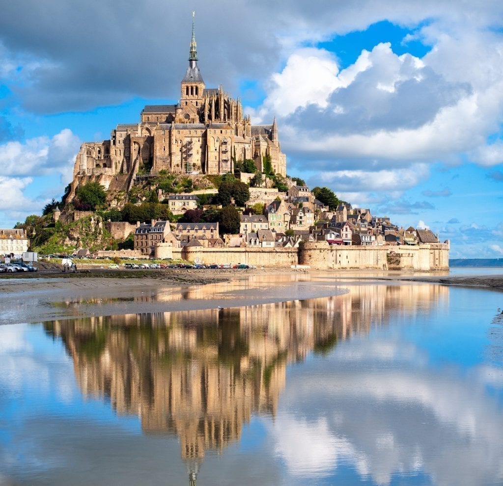 Mont St. Michel in northern France with its reflection showing in the water in the bottom half of the photo