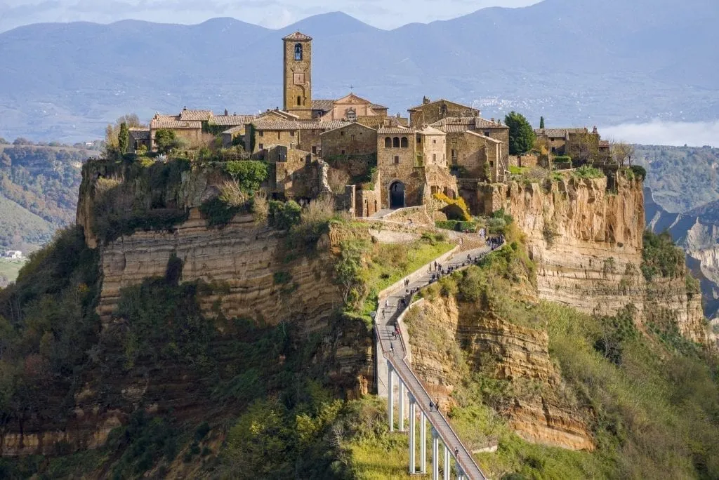 Civita di Bagnoregio as seen from across the gorge from town with pedestrain bridge in the center of the photo. One of the best independent day trips from Rome Italy