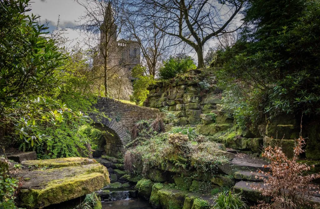 historic stone bridge in a glen with church in the background in east scotland