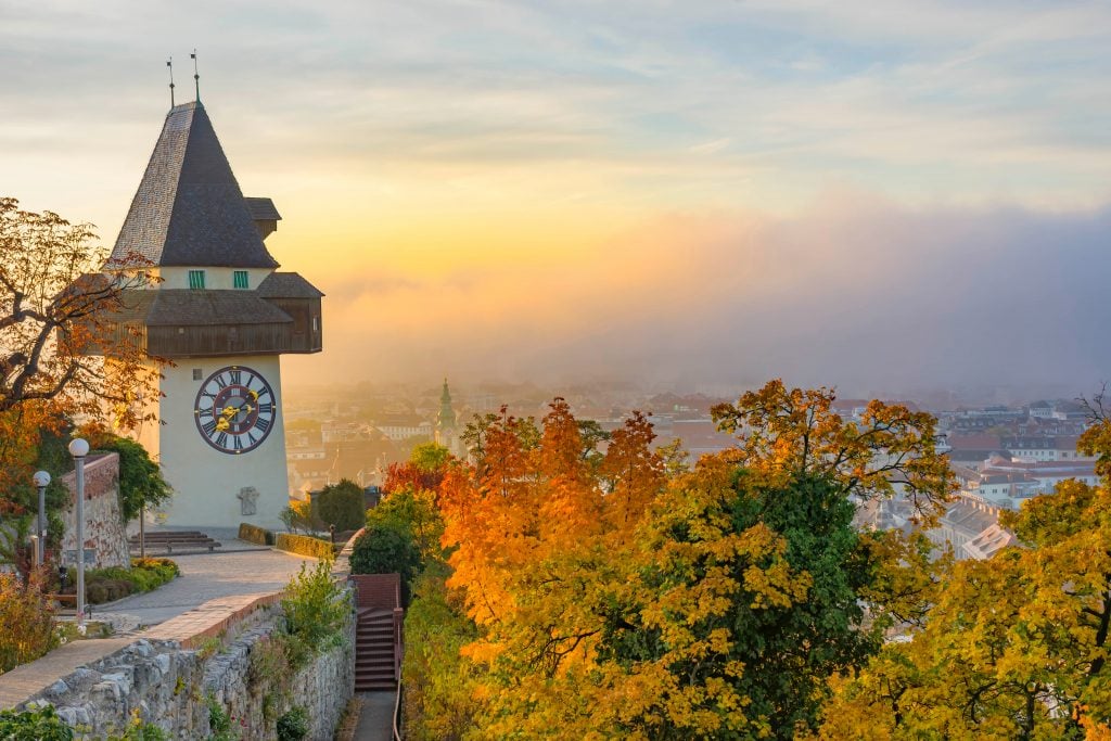 clock tower of graz austria at sunset with fall foliage in the foreground