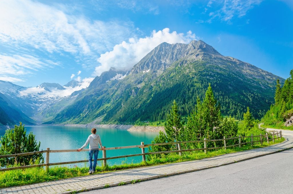 woman standing in front of bright turqouise lake in the austrian alps, one of the best road trips europe