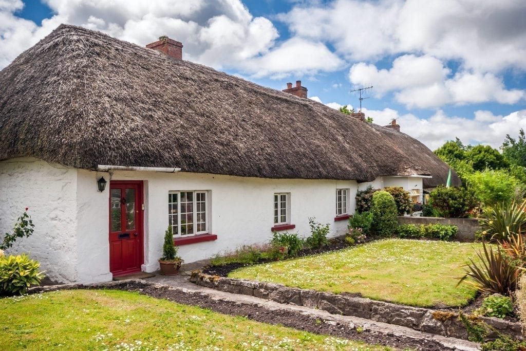 Thatched roof cottages in Adare Ireland with white walls and a red door. Adare is one of the best small towns in Ireland