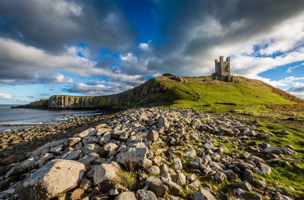 Dunstanburgh castle england in the distance with rocky landscape in the foreground