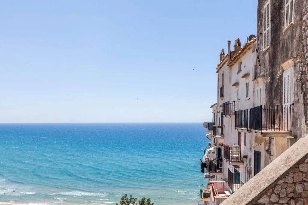 View of Sperlonga Italy, one of the most fun day tours from Rome Italy, with the town visible on the right and the bright blue water of the sea taking up most of the photo