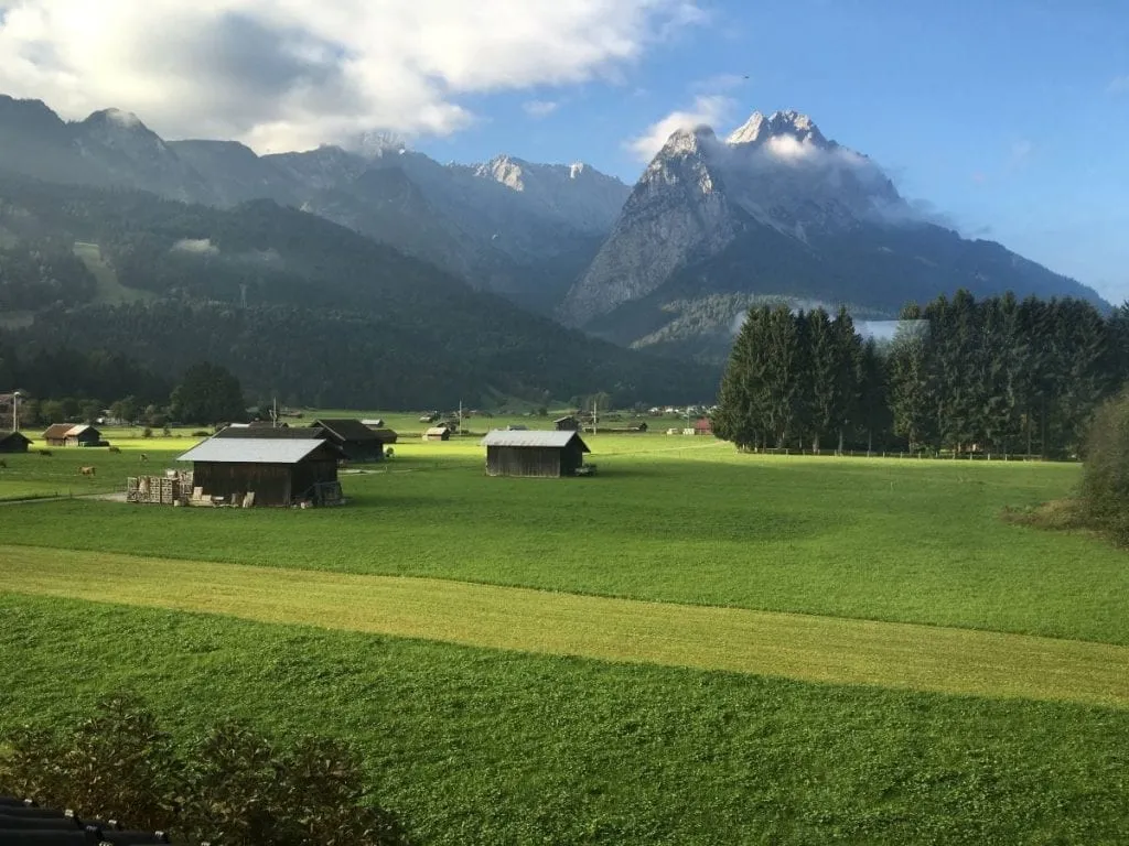 Garmisch Germany, expansive green field with a few houses framed by mountains in the background