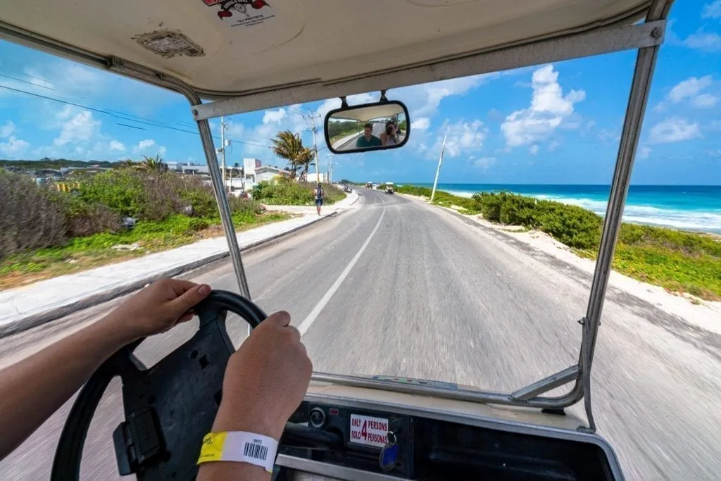 Jeremy's hands steering a golf cart down the empty road in Isla Mujeres. Renting a golf car is one of the best things to do in Isla Mujeres