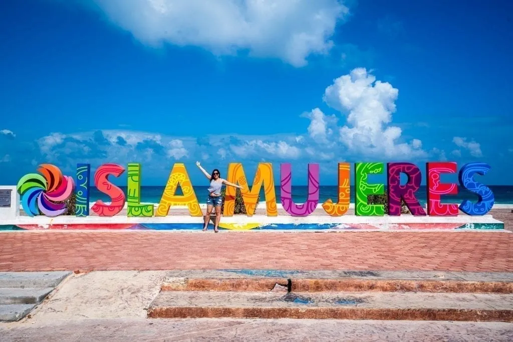 Kate Storm standing in front of colorful Isla Mujeres sign, one of the fun places to visit in Isla Mujeres Mexico