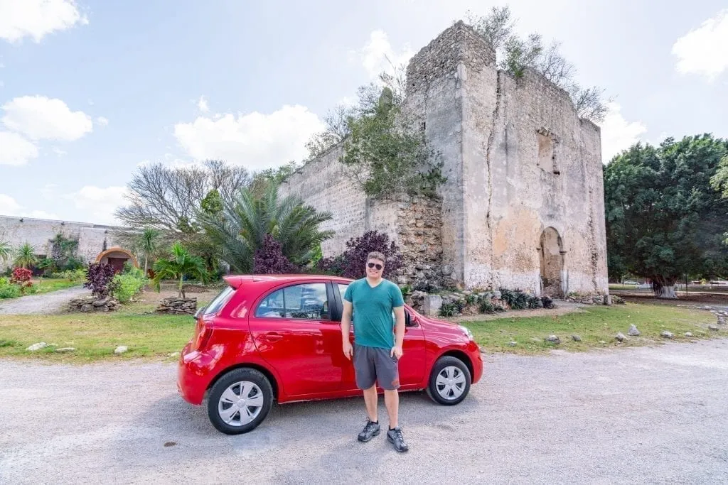 Jeremy Storm standing in front of a red car parked in front of a church as part of a road trip Yucatan itinerary