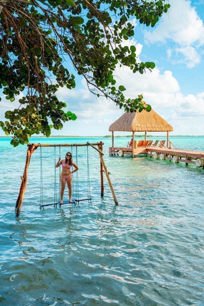 kate storm standing on an overwater swing in bacalar mexico