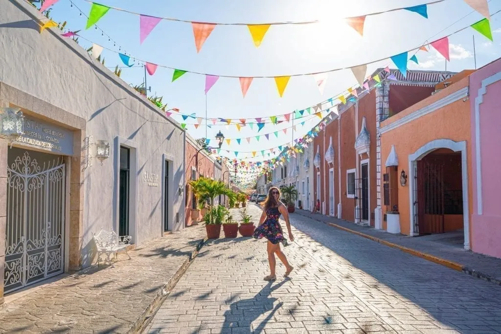 Kate Storm standing on a colorful street with flags hanging over it in Valladolid Mexico during a Yucatan road trip