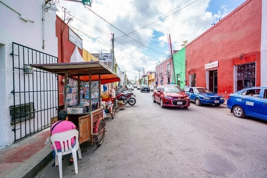 colorful street in valladolid with some cars on it and a street food stall to the left