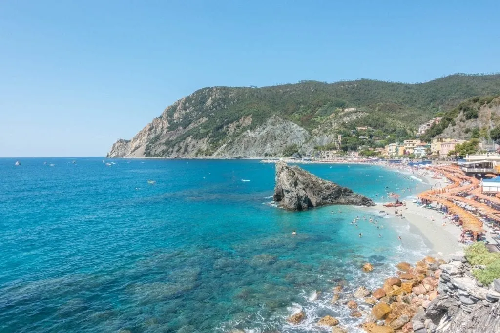 View of Monterosso al Mare beach from above on a sunny day, umbrellas are visible on the right side of the photo. This beach is one of the most instagrammable places in Cinque Terre!