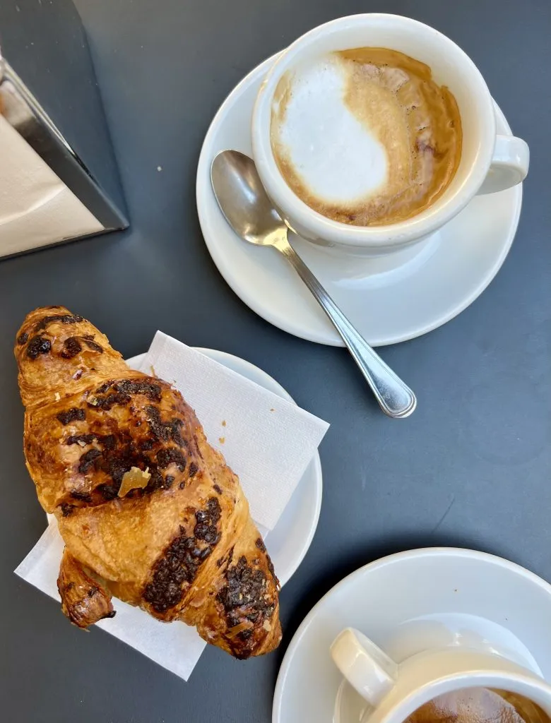 photo of a coffee and croissant on a table at an italian coffee bar
