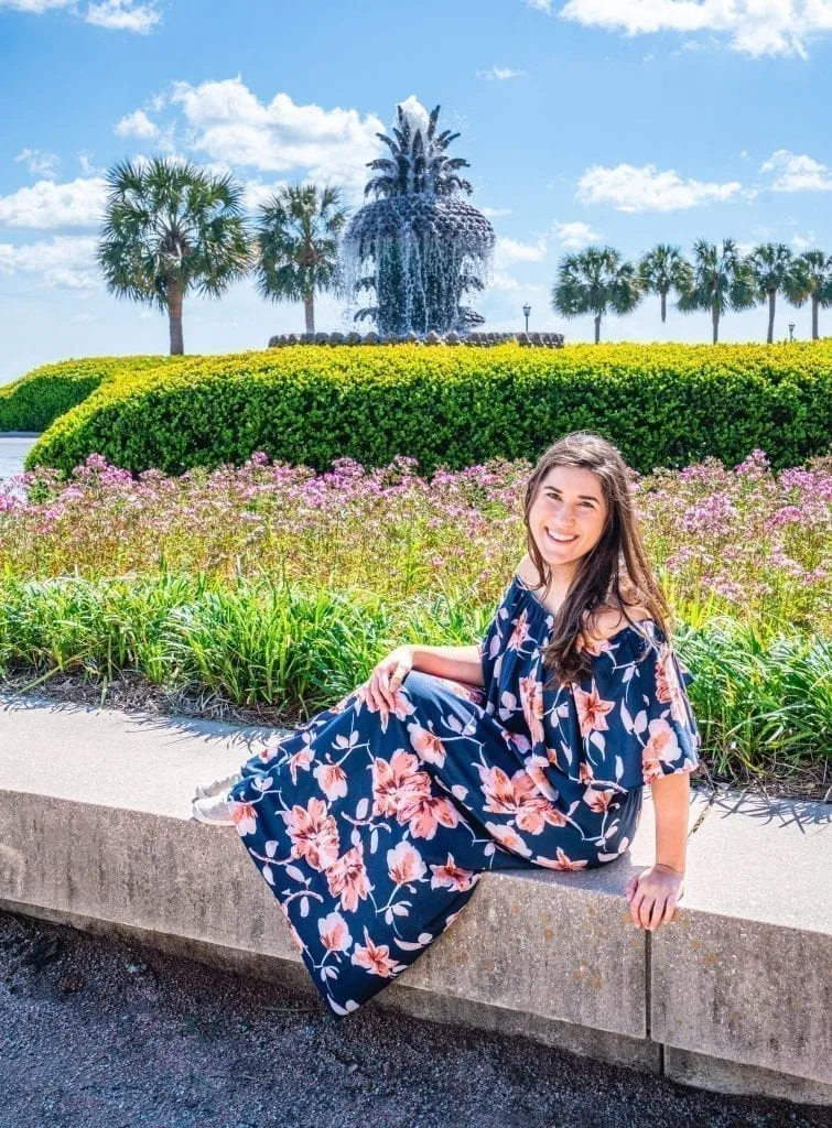Kate Storm sitting in front of the pineapple fountain in Charleston SC--choosing whether to visit Savannah or Charleston is no easy task, but we wrote this guide to help!