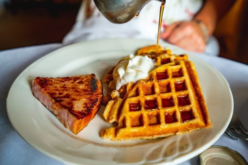 Pecan waffles with syrup being drizzled on them in Savannah GA, as seen on a weekend getaway by the author of this Savannah blog post