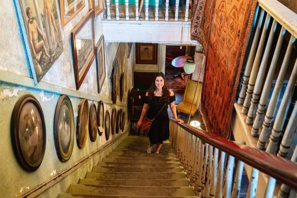 Kate Storm in a black dress standing on a staircase in Alex Raskin Antiques during a long weekend in Savannah GA