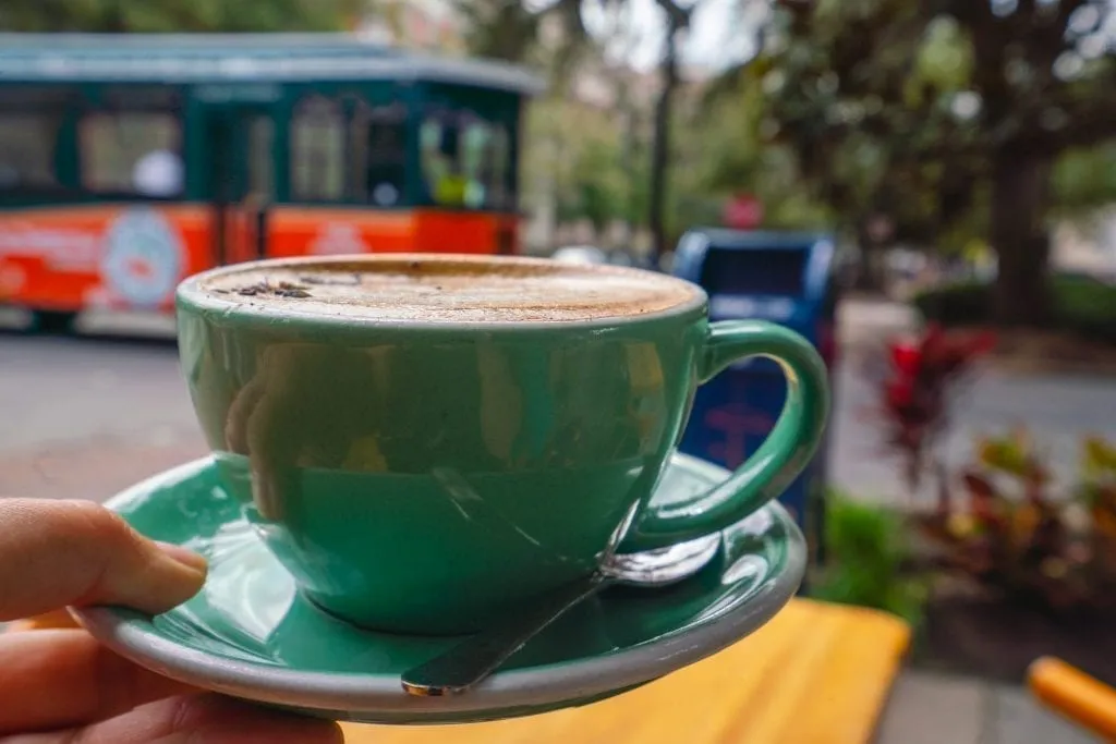 Spiced lavender mocha in a green mug being held up in front of a Savannah trolley. Coffee is from The Collins Quarter, one of the best Savannah photography locations