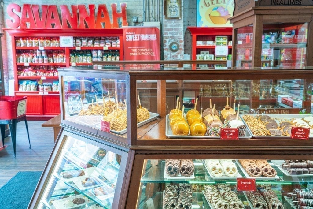 Interior of Savannah Candy Company with a case of candy in the foreground and a red bookshelf with savannah written on top in the background