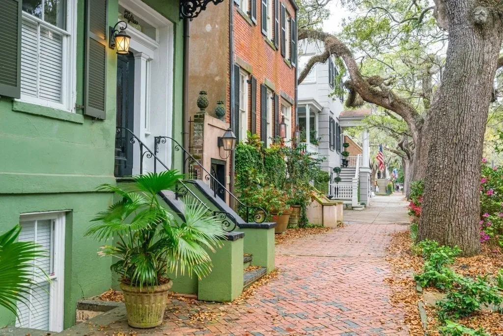 Jones Street in Savannh GA with a green house in the left foreground and an oak tree on the right. Jones Street is one of the best Savannah photo spots