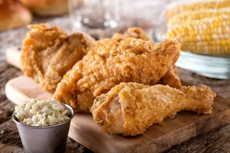 Plate of fried chicken with coleslaw on the left side and corn in the background, one of the best Lowcountry foods to eat