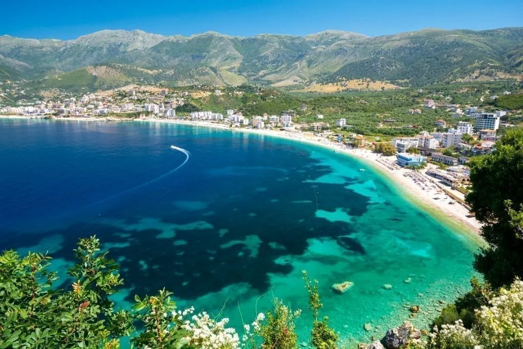 Albanian Riviera as seen from above with a boat in the distance and mountains in the background, one of the best places to vacation in Europe summer