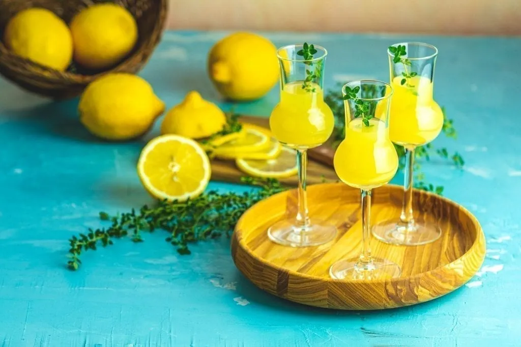 limoncello served in 3 glasses with lemons in the backgorund, one of the best italy souvenirs