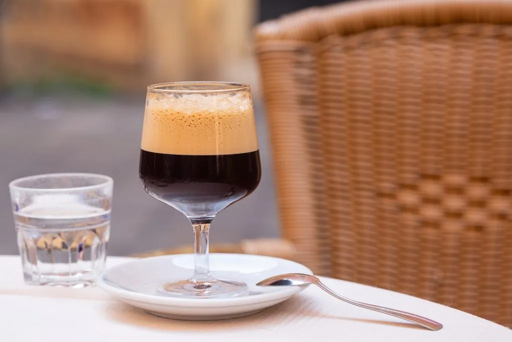 a caffe shakerato sitting on an italian cafe table with a glass of water next to it