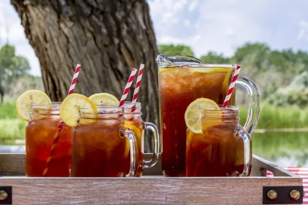 4 mason jars of sweet tea with lemon in front of a pitcher, one of the best drinks in Savannah GA