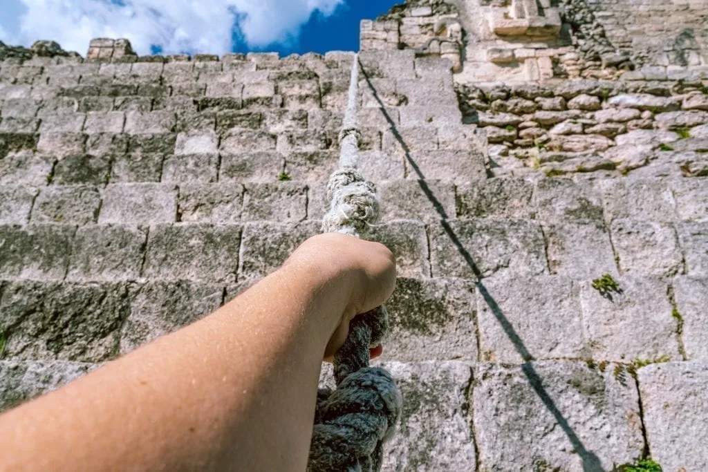 Jeremy Storm's arm reaching out and holding a rope to scale a pyramid in Becan Mayan City Mexico